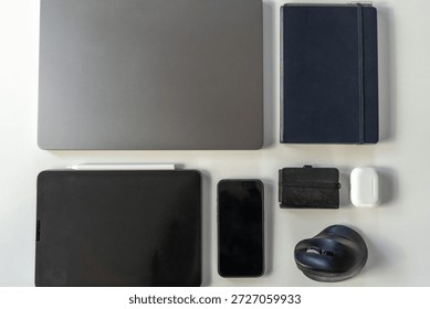 Close up of clean flat lay of everyday technology items showing portable electronics, stationery, and accessories arranged symmetrically on a white surface.
