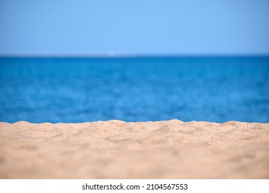 Close Up Of Clean Yellow Sand Surface Covering Seaside Beach With Blue Sea Water On Background. Travel And Vacations Concept.