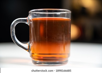 Close Up Of Clear Glass Cup Mug Of Rich Fresh Ceylon Black Tea On A White Table With Dark Out Of Focus Blurred Bokeh Background