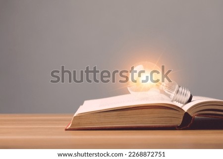 Close up clear light bulb with light effect on old book and put on wooden desk with grey space wall background. Idea of learning, Education concept.