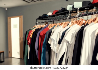 Close Up Of Clothes Rack Or Rail With Baseball Caps And Other Apparel In The Store. Items At Custom T-shirt, Clothing Printing Company. Horizontal Shot. Selective Focus