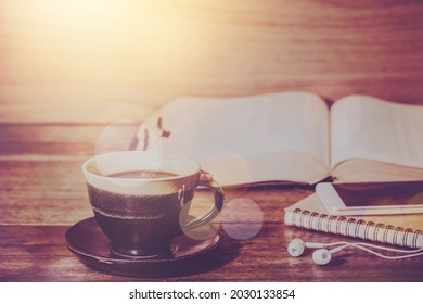 Close up of a coffee cup and s mall note book with earphone over blurred open bible on a wooden table background, Christian education, bible study or devotional concept with copy space, spirituality