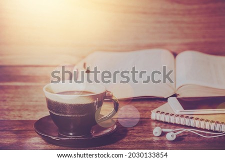 Close up of a coffee cup and s mall note book with earphone over blurred open bible on a wooden table background, Christian education, bible study or devotional concept with copy space, spirituality
