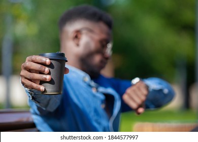 Close up of a coffee cup stretched by a busy african office worker looking at his watch