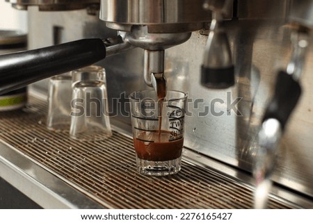 Close up of coffee dripped into small cup from coffee machine made from crome stainless steel.