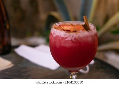 Close up of a cold red aromatic seasonal cocktail made with berries, cinnamon, and spices served in a beautiful round frosted glass cup. Blurred rustic background. Specialty drinks and unique flavors. - Shutterstock ID 2104133330