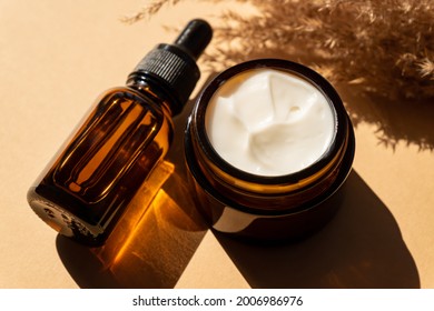 Close Up Of Collagen Cream In Glass Jar, Serum In Amber Glass Bottle And Dry Flowers Reeds On Beige Background. Set For Skin And Body Care Beauty Products.