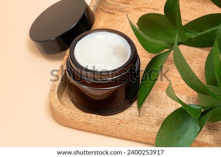 close up of collagen cream in glass jar and green leaves on beige background. skin and body care beauty products. Mockup.