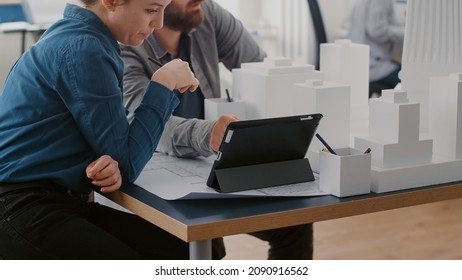 Close up of colleagues working with tablet and building model to design construction layout. Man and woman looking at digital device and analyzing maquette for urban development. - Powered by Shutterstock