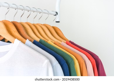 close up a collection of pastel color t-shirts hanging on a wooden clothes hanger in closet or clothing rack over white background, copy space