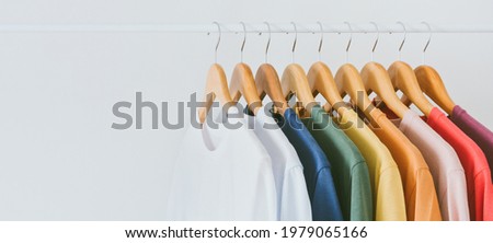 Close up a collection of pastel color t-shirts hanging on a wooden clothes hanger in closet or clothing rack over white background, copy space