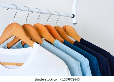 close up collection shade blue tone color t  shirts hanging wooden clothes hanger in closet clothing rack over white background and copy space