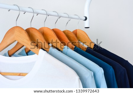 close up collection shade of blue tone color t-shirts hanging on wooden clothes hanger in closet or clothing rack over white background with copy space