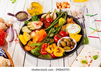 Close Up Of Colorful Grilled Vegetable Bounty Tray On Cast Iron Pan With Olives And Dip Resting On White Painted Wooden Picnic Table