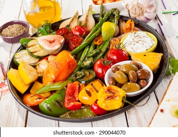 Close Up Of Colorful Grilled Vegetable Bounty Tray On Cast Iron Pan With Olives And Dip Resting On White Painted Wooden Picnic Table