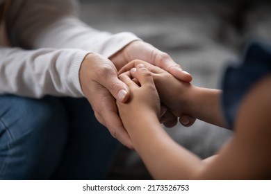 Close up compassionate young foster parent holding hands of little kid girl, giving psychological help, supporting at home. Sincere different generations family sharing secrets or making peace. - Shutterstock ID 2173526753