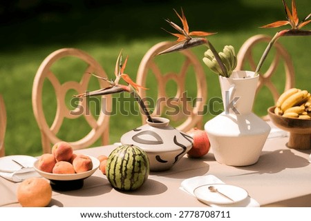 Close composition of elegant outdoor table decor with fruits, sculptural ceramics and tropical strelitzia flowers, modern aesthetic emphasizing texture, balance and curated summer event styling