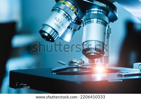 close up of compound microscope with ray of orange light shining in lab setting show scientific equiptment
