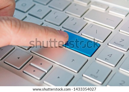 Close up of computer laptop keyboard with a blank blue button for any message and copy space. Conceptual image of an alert, danger, warning, announcement, etc. The man's finger presses the button.