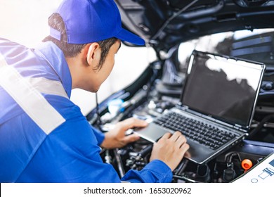 Close up concept of male asian car mechanic using a computer laptop to diagnosing and checking up on car engines parts for fixing and repair, working on the car engine wearing blue overall and a hat - Powered by Shutterstock - Get 15% off with code: PIKWIZARD15