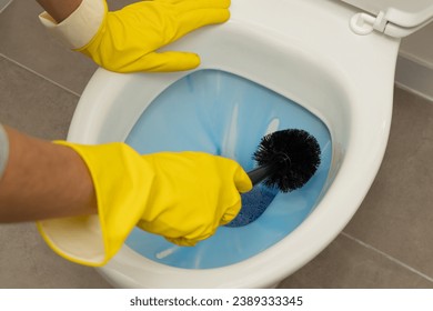 Close up concept shot of a hands cleaning a toilet with a toilet brush and toilet cleaner, wearing yellow gloves