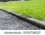 Close up of concrete lawn edging (curbing) bordering an asphalt driveway. A detail highlighting the effectiveness of the curbing, and contrasts the green lawn with the dark tarmac. 