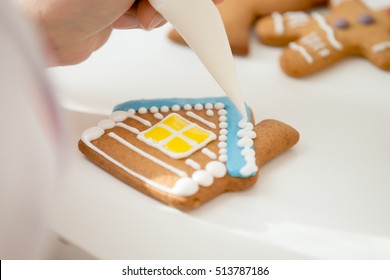 Close up of confectioner hand decorating a gingerbread house, the roof with icing sugar for a snowy effect using a pastry bag. View over a shoulder, lifestyle - Powered by Shutterstock