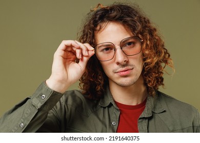 Close Up Confident Calm Frowning Displeased Pensive Long Curly Hair Young Brunet Man 20s Wears Khaki Shirt Jacket Touch Glasses Looking Camera Isolated On Plain Olive Green Background Studio Portrait