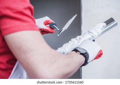 Close Up Of Construction Male Worker Applying Thin Coat Of Drywall Compound Using Professional Taping Knife.