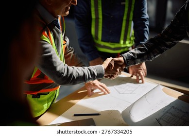 Close up of construction worker and architect handshaking at building site. 