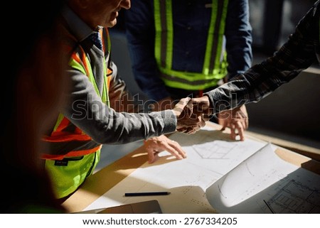 Close up of construction worker and architect handshaking at building site. 