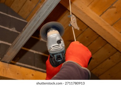 Close up of a construction worker using an angle grinder above his head to cut or polish a metal bar in an attic, capturing a precise renovation moment inside a partially finished home.