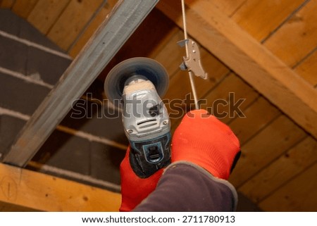 Close up of a construction worker using an angle grinder above his head to cut or polish a metal bar in an attic, capturing a precise renovation moment inside a partially finished home.