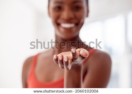 Close up of contact lens on finger of young african woman. Mature black woman holding contact lens in front of her face. Happy smiling woman showing contact lens.