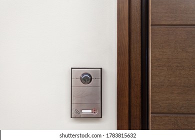 Close Up Of Contemporary Doorbell Near Door With Security Panel, Intercom And Video Camera In Modern House Against White Copy Space Wall