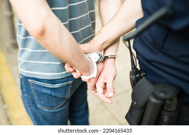 Close up of a cop agent making an arrest and young man with handcuffs going to the police station for commiting a crime