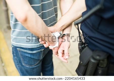 Close up of a cop agent making an arrest and young man with handcuffs going to the police station for commiting a crime