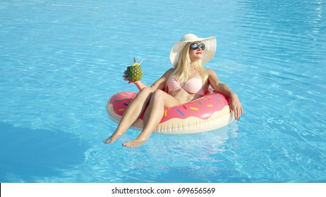 CLOSE UP COPY SPACE Happy Young Woman On Summer Vacation Lying On Inflatable Doughnut Floatie In Pool, Drinking Pineapple Alcohol Beverage. Smiling Girl Floating On Inflatable Pillow & Sipping Drink