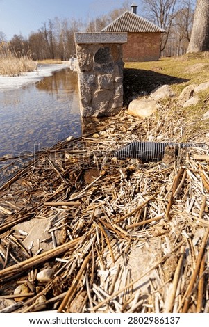 Close up of a corrugated plastic drainage pipe pouring clean water into a lake near a stone embankment during early spring thaw.