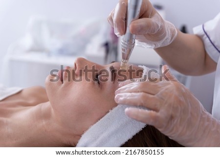 close up of Cosmetologist,beautician applying facial dermapen treatment on face of young woman customer in beauty salon.Cosmetology and professional skin care, face rejuvenation.