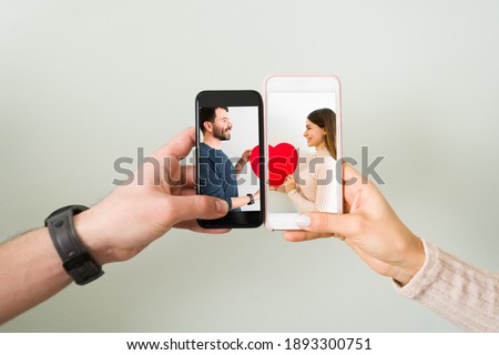 Close up of couple joining two smartphones together with a photo of an attractive man and young woman in love holding a red heart. Love concept