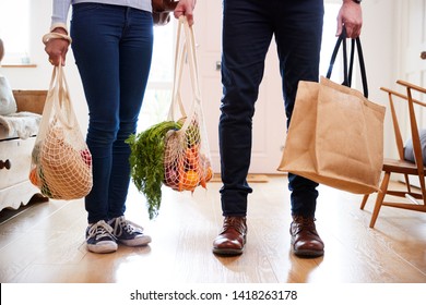 Close Up Of Couple Returning Home From Shopping Trip Carrying Groceries In Plastic Free Bags