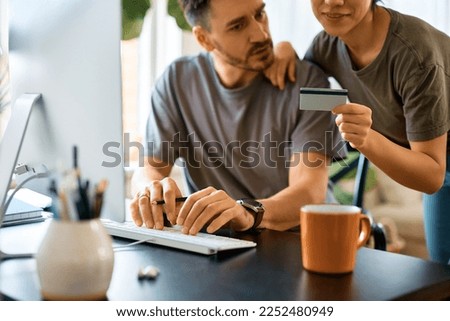 Close up of couple using credit card and computer while checking their online bank account at home.