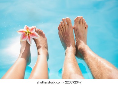 Close Up Of Couple's Bare Feet Against Swimming Pool On A Sunny Day