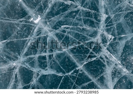 Close up of cracked ice patterns on a frozen lake, showing blue tones, fractures and natural texture. Winter background with copy space for design and banners
