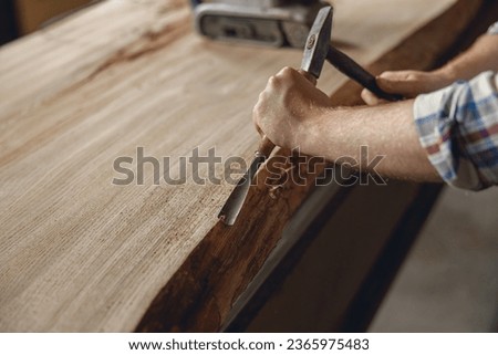 Close up of craftsman working with chisel while cutting wooden plank in carpentry workshop