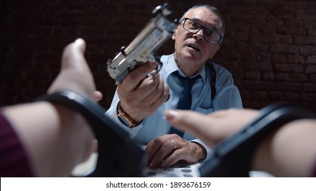 Close Up Of Criminal Hands In Handcuffs And Police Officer Threatening With Gun During Interrogation. Senior Detective Holding Pistol And Questioning Arrested Person