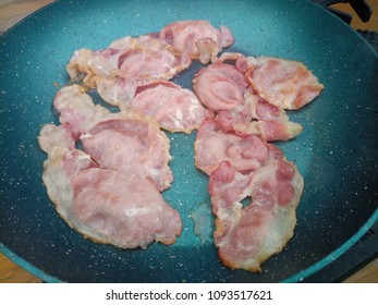 Close up of crispy bacon frying in a hot oily non-stick pan 