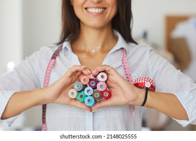 Close Up Crop Of Happy Successful Female Seamstress Make Heart Hand Gesture With Threads Love Dressmaking Business. Smiling Woman Designer Or Tailor Affectionate About Fashion And Style Atelier.