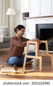 Close up crop narrow view of young Indian woman gather wooden shelf or chair sit on floor in living room. Ethnic female renter put together construct piece of furniture settle in new home or house.
